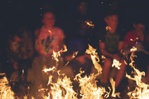 people sitting around a campfire with flames 