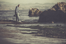A man walking along a rocky shore. 