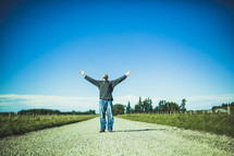 man standing in the middle of a road with hands raised to God 