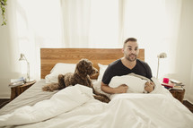 Awake man sitting up in bed with dog.