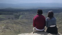 couple sitting on the edge of a mountain looking out and enjoying the view 