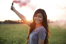 young woman holding a smoke flare at sunset 