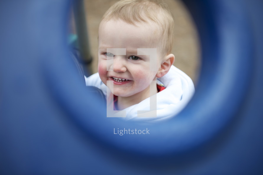 A baby seen through a playground window.
