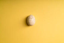 white speckled Easter egg on a yellow background 