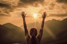Rear view of woman with hands up in worship against beautiful sunset over mountains