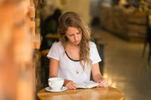 a woman sitting on a table in a cafe reading a Bible 