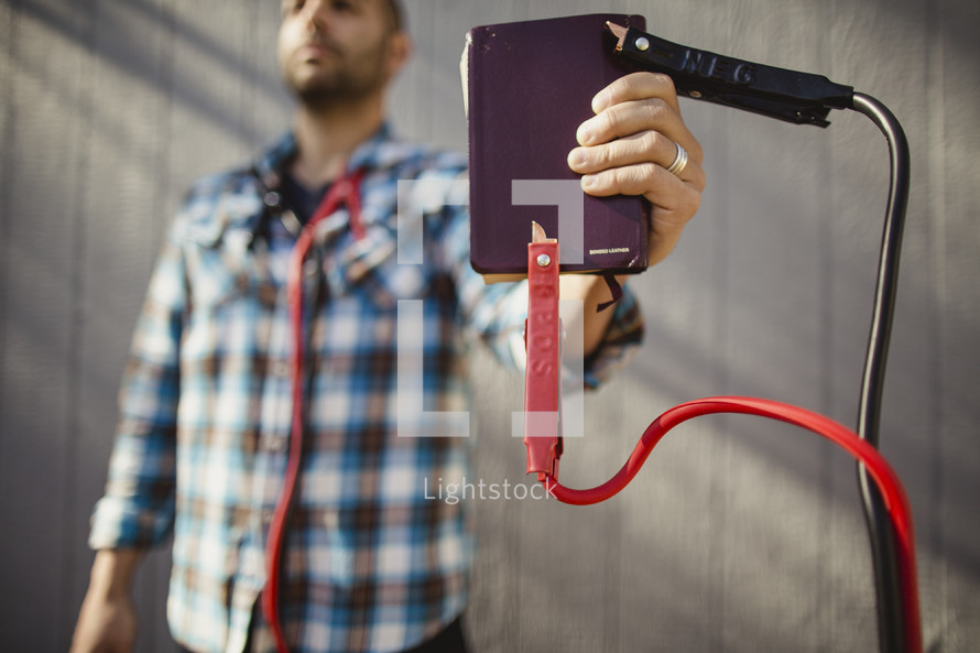 Man holding Bible with jumper cables attached.