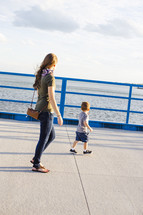 a mother and son walking on a harbor sidewalk 
