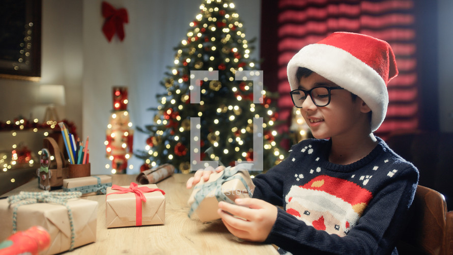 Kid With Christmas hat looking at presents on his desk 
