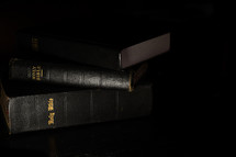 stack of three Bibles on a black background 