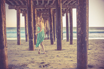 A woman walking in the sand under a pier.