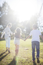 siblings walking holding hands through grass 