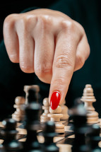 Woman player playing board intelligence game - wooden chess. Close- up view of female arm with red nails moves a chess piece pawn, first move. Sport, success strategy concept. High quality