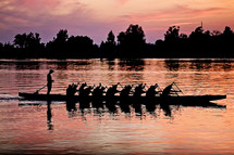 silhouette of rowers paddling a boat at sunset 