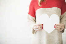 Woman in a red and white sweater holds a white paper heart.