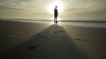 a man walking on a beach at sunrise 