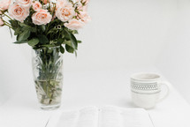 open Bible, coffee cup, and flowers in a vase on a white background 