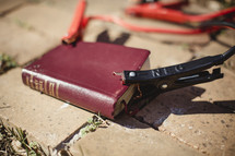 Red Bible laying on brick sidewalk with jumper cables attached.