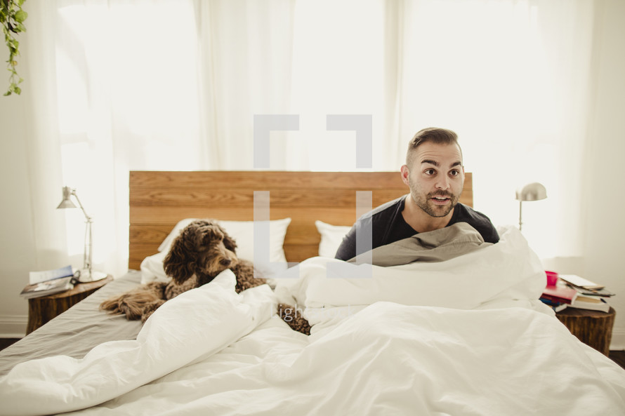 Suprised man sitting up in bed with dog.