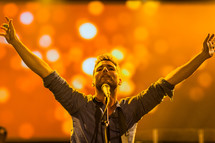 A man at a microphone with arms raised worship leader passion singing 