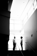 man and woman standing at the top of stairs talking 