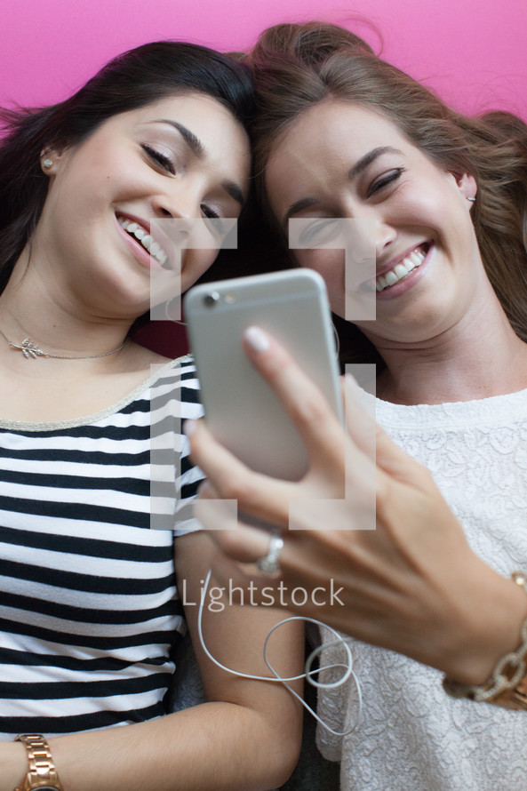 Two young women smiling and looking at a cell phone.