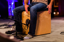 Man in socks sitting on cajon wooden drum box on stage playing hitting percussion