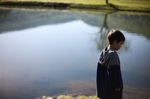 a boy child standing at the edge of a pond 