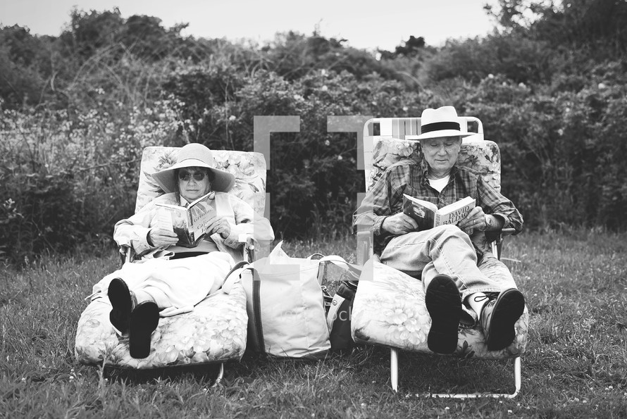 elderly couple reading together in lawn chairs