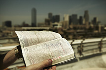 A man stands on the rooftop with an open Bible in hand overlooking the city of Dallas.