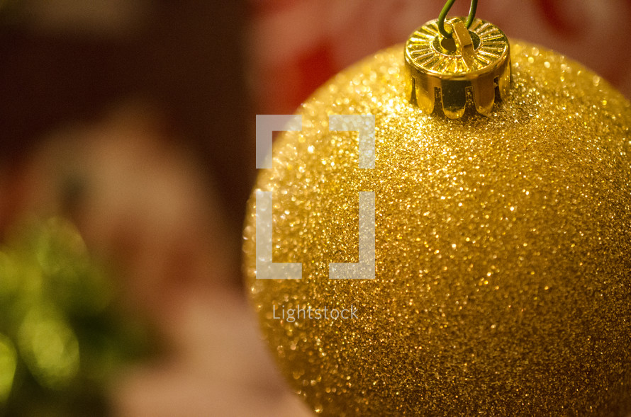 Gold glitter ball ornament hanging on Christmas tree.