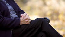 Worried senior woman rubbing her hands on bench in park outdoors closeup.