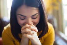 a Latino woman sitting on a couch with praying hands 