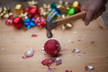 Hand holding a hammer, smashing a Christmas ornament on a wood board.