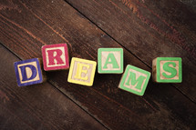 The word "dreams" spelled out with colorful wooden children's blocks.