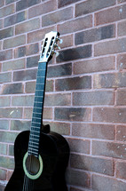 black acoustic guitar against a brick wall 