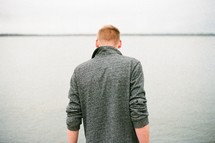 a man with his back to the camera standing by a lake 