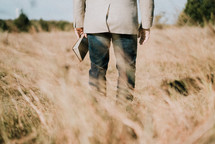 a man standing in a field holding a Bible at his side 