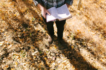 a man standing in fall leaves reading a Bible 