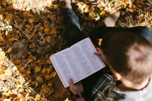 man sitting in fall leaves reading a Bible