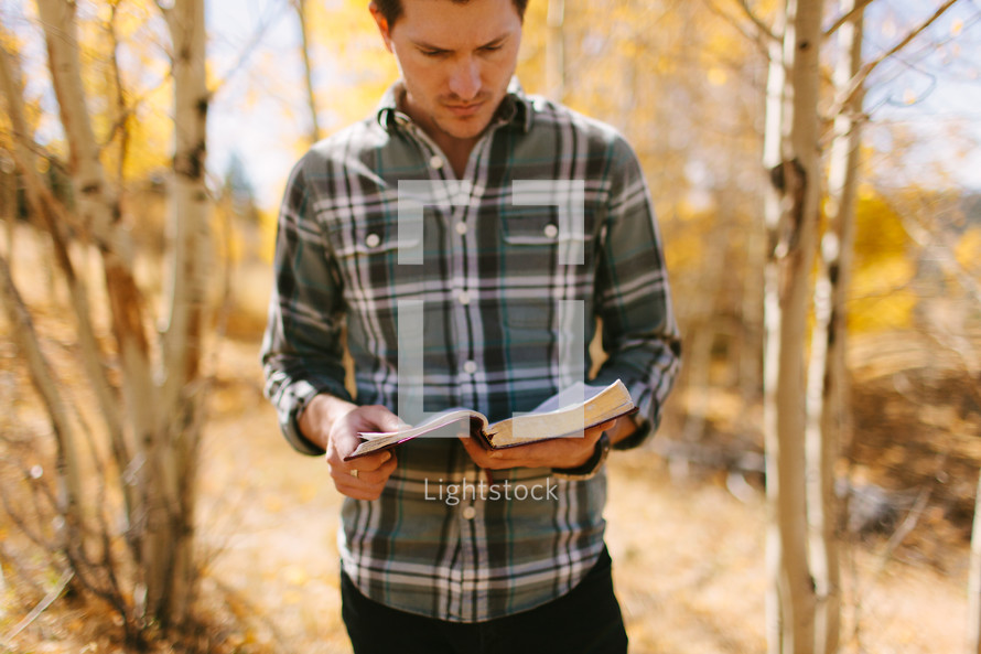 a man standing alone in a fall forest reading a Bible 