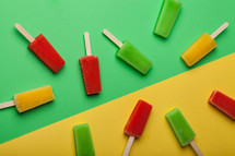 Brightly colored popsicles randomly arranged on a green and yellow background.