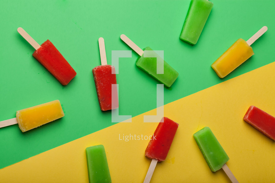 Brightly colored popsicles randomly arranged on a green and yellow background.