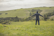 a man standing with outstretched arms in a field of green grass 
