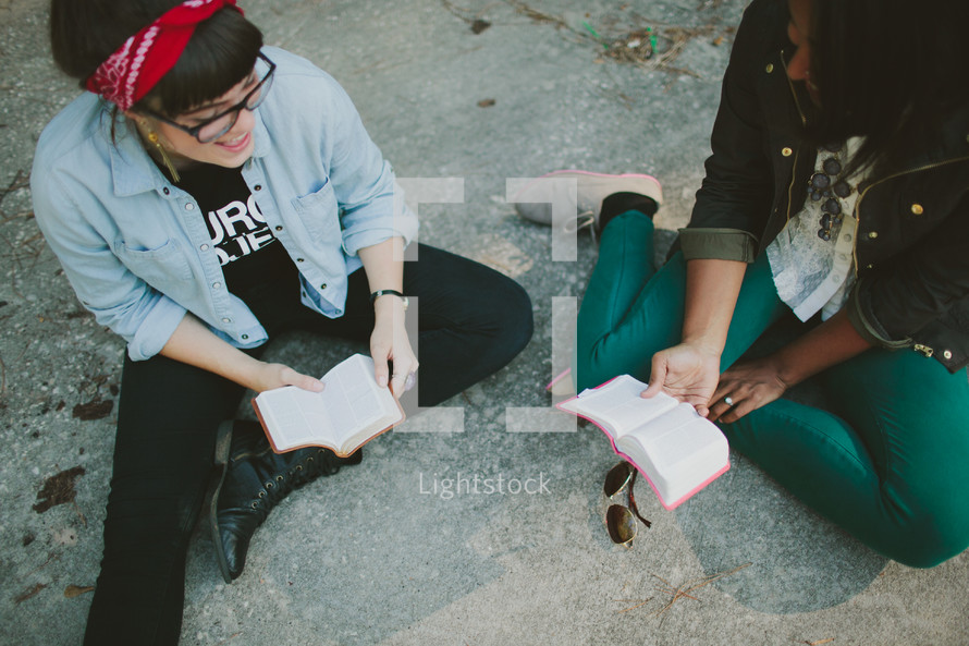Friends sitting on ground reading Bible