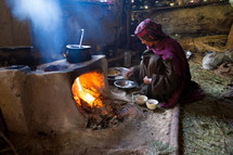 A woman cooking at a clay stove in a hut 