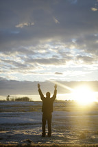 man standing with raised arms in a snow covered field 
