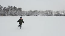 Drone shot of young boy playing in the snow on a winter, overcast day.