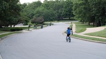 Kids ride their bikes through the neighborhood. Riding away from camera.