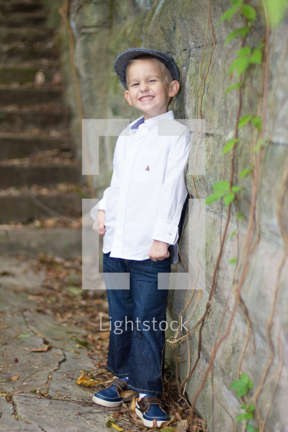 A smiling boy leaning against a rock wall.